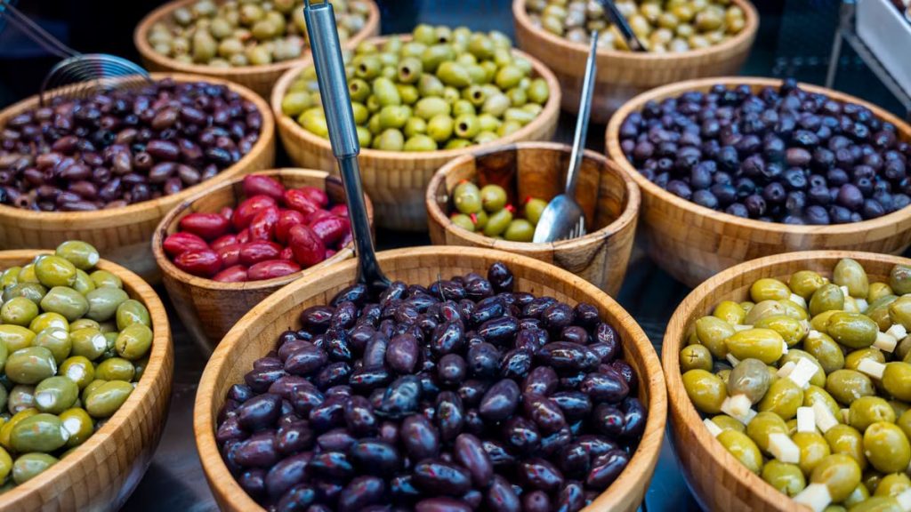 Various types of olives displayed in wooden bowls at an outdoor market.