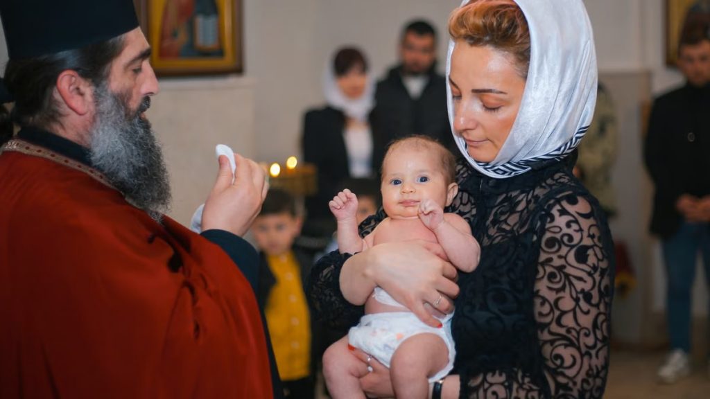 A mother holding her baby during a baptism ceremony with a priest inside a church.